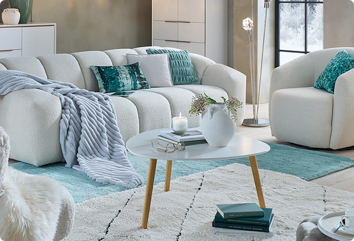 Weiße Polstermöbel, weißer Couchtisch und weiße Kommode sowie Highboard mit weißen, grünen und grauen Wohnaccessoires im Wohnzimmer