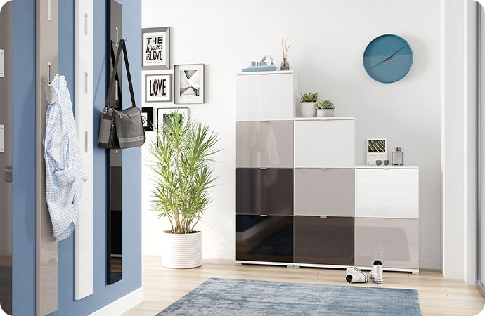 Flur mit Garderobenpaneelnen in Grau, Hellgrau, Weiß und Schwarz vor blauer Wand sowie Schuhschank in Treppenform mit Hochglanz-Fronten in Grau, Hellgrau, Weiß und Schwarz