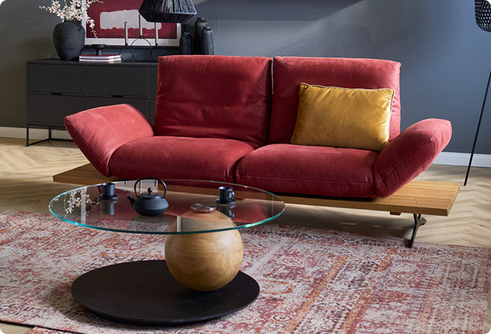 Wohnzimmer mit rotem Ledersofa, einen runder Glastisch und einer schwarzen Kommode mit Dekoration.