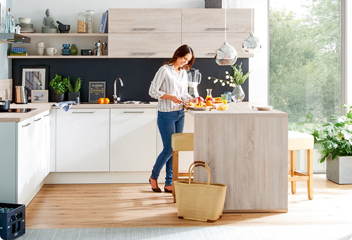 Küche in U-Form in Weiß und Holzoptik, Frau die am Küchentresen steht und Essen zubereitet