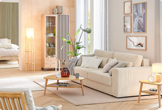 Wohnzimmer mit cremefarbigem Cordsofa, Holz-Couchtisch, Holz-Vitrine und weiteren Möbeln und Deko