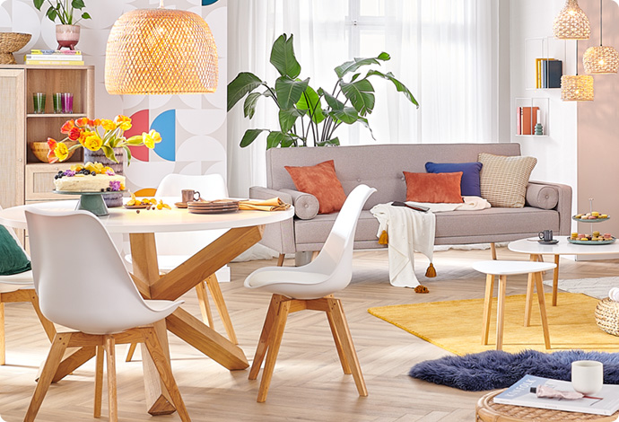 Essgruppe bestehend aus rundem, weißem, gedecktem Tisch mit Holzgestell und weißen Schalenstühlen mit Holzgestell, Rattan-Pendelleuchte, im Hintergrund ein graues Sofa