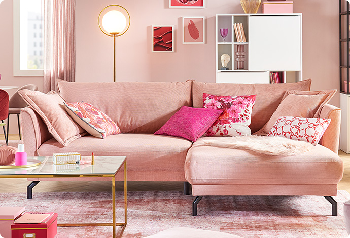 Rosa Ecksofa mit Kissen in Pink- und Rosatönen, weißer Couchtisch mit Gestell in Gold, Deko und weitere Möbel in rosa Wohnzimmer