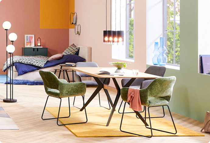 Holz-Esstisch mit schwarzem Gestell und Polsterstühle in Grün und Grau auf gelbem Teppich, Pendelleuchte aus schwarzem Rauchglas