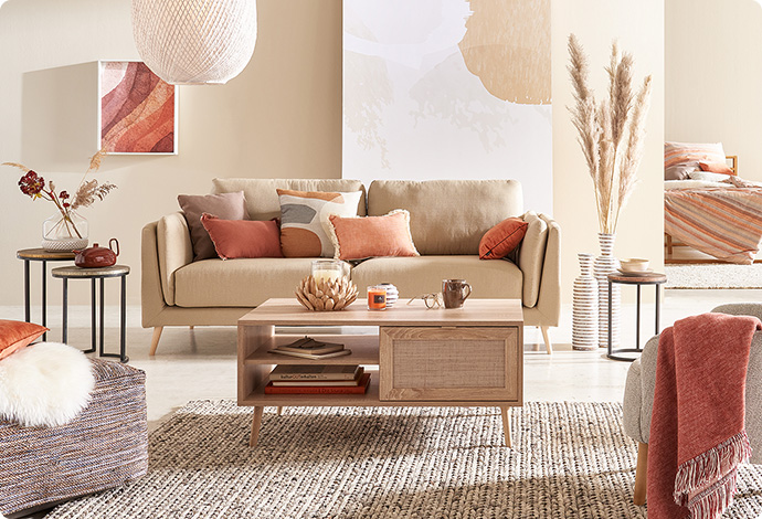Couchtisch in Holz- und Rattanoptik auf Naturteppich, beiges Sofa mit Kissen in Naturtönen in einem Wohnzimmer