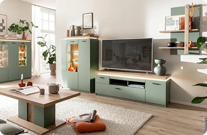 Wohnzimmer mit salbeigrünen & holzfarbigen, beleuchteten Möbel, bestehend aus 2 Highboards, TV-Board, Wandregal, Couchtisch, Deko.