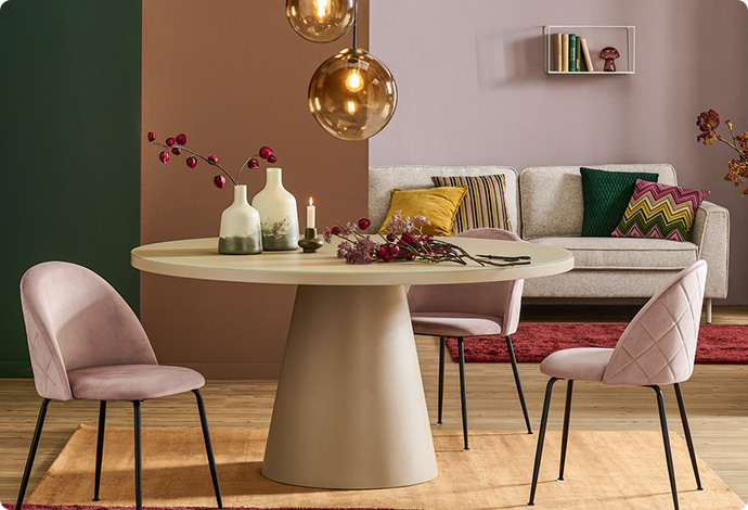 Runder, beiger Esstisch, zwei rosa Polsterstühlen und Herbstdeko auf dem Tisch