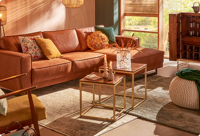 braunes Leder-Ecksofa, 2 Couchtische aus Holz und goldfarbigem Metall, gelber Sessel mit Holzakzenten in einem Wohnzimmer