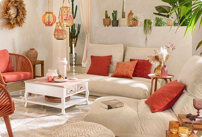 Wohnzimmer mit zwei beigen Relaxliegen, terrakotta-farbene Kissen, Bodenkissen in Creme, weißer Couchtisch mit holzfarbener Tischplatte, bunte und weiße Glas- und Keramikaccessoires 