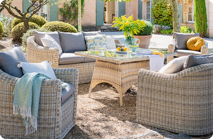 Gartenserie Sylt aus beigem Polyrattan mit passenden Auflagen - Gartentisch, 2 Gartensofas und 2 Gartensessel - alle in einem Garten - Tisch ist gedeckt