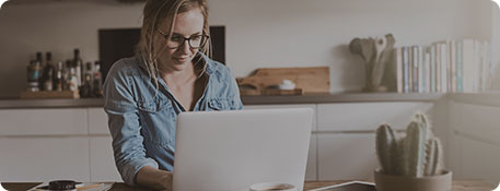 Frau an Laptop in Küche mit weißer griffloser Küchenzeile in L-Form