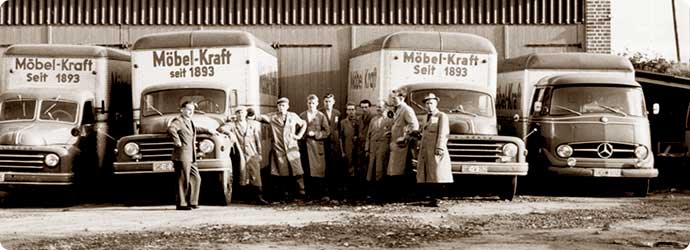 Historische Fotografie in Schwarz/Weiß mit Mitarbeiten vor LKW-Flotte, LKW mit Aufdruck Möbel Kraft seit 1893