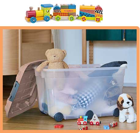 Transparente Aufbewahrungsbox gefüllt mit Kuscheltieren. Davor liegt eine Holzeisenbahn