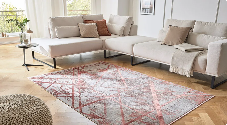 Wohnzimmer mit cremefarbigem Ecksofa und rot-grau geometrisch gemustertem Teppich, weitere Möbel und Deko