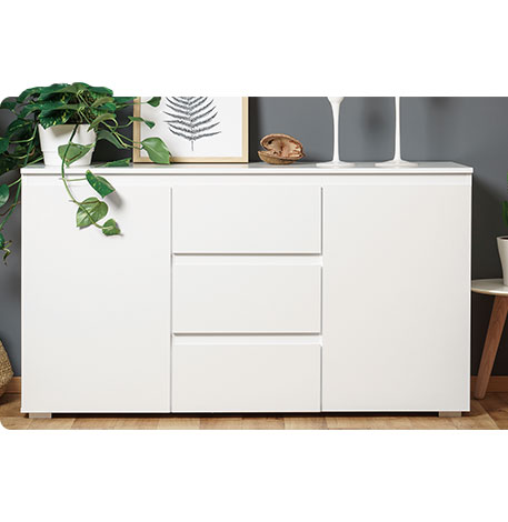 Weißes Sideboard mit 2 Türen und mittig 3 Schubladen - darauf stehend eine grüne Pflanze mit weißem Topf, ein Bild und weitere Deko - teilweise freigestellt oben