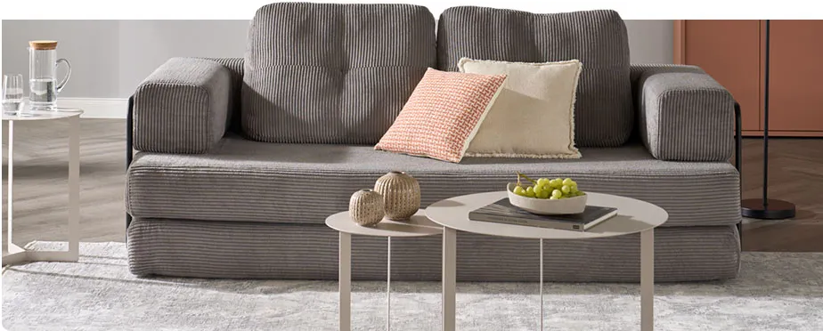 Wohnzimmer mit grauem Cordsofa, hellgraue runde Couch- bzw. Beistelltische, Deko. Hinweis: Wohnfertig in Minuten