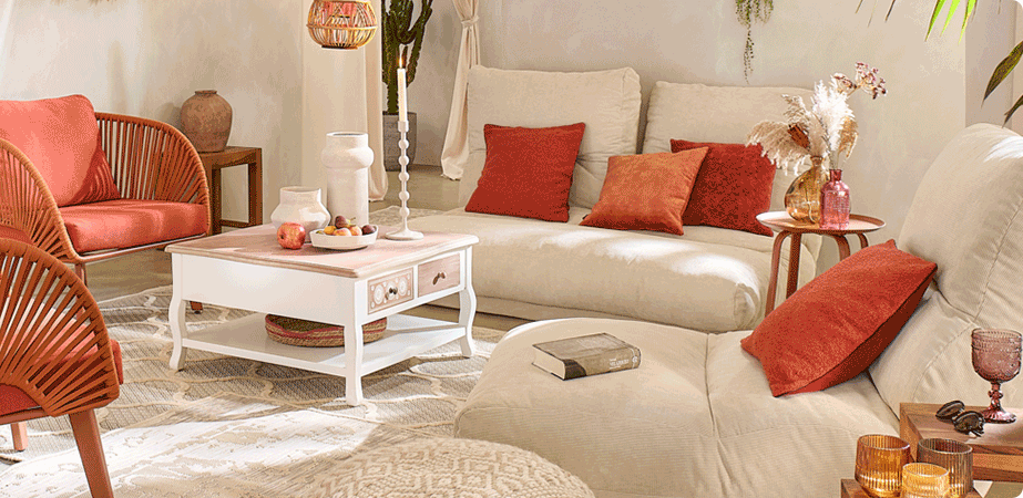Wohnzimmer mit zwei beigen Relaxliegen, darauf terrakotta-farbene Kissen. Terrakottafarbene Sessel, Bodenkissen in Creme, weißer Couchtisch mit holzfarbener Tischplatte. Braune  und weiße Glas- und Keramikaccessoires 