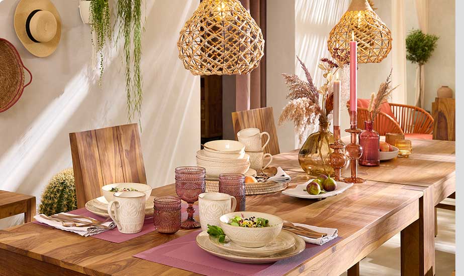 Esszimmer mit einer Tischgruppe, Esstisch und Stühle in dunklem Holz. Frühstücks- und Tafelservice in Beige, rosafarbenen Trinkgläser, braunen und rosafarbenen Glasvase, Kerzenständer, Windlichtern, Deckenlampe aus Rattan
