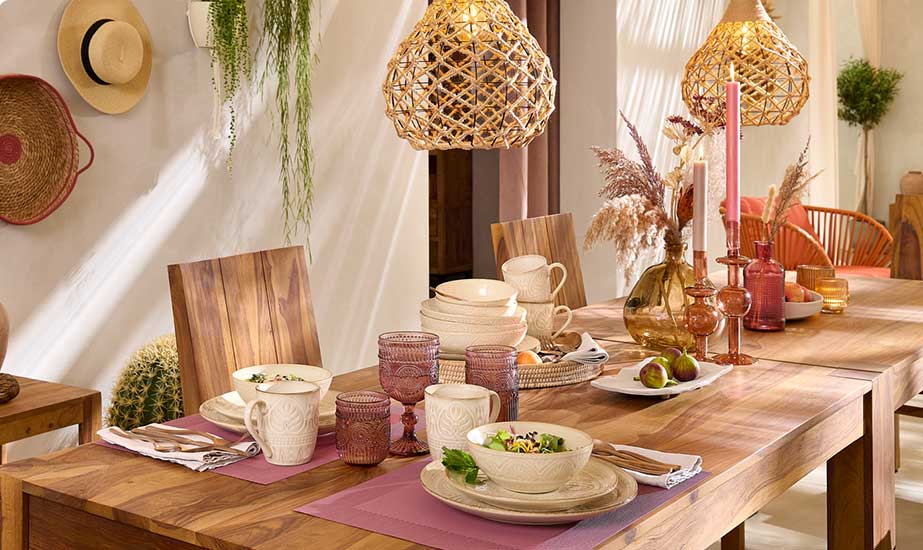 Esszimmer mit einer Tischgruppe, Esstisch und Stühle in dunklem Holz. Frühstücks- und Tafelservice in Beige, rosafarbenen Trinkgläser, braunen und rosafarbenen Glasvase, Kerzenständer, Windlichtern, Deckenlampe aus Rattan
