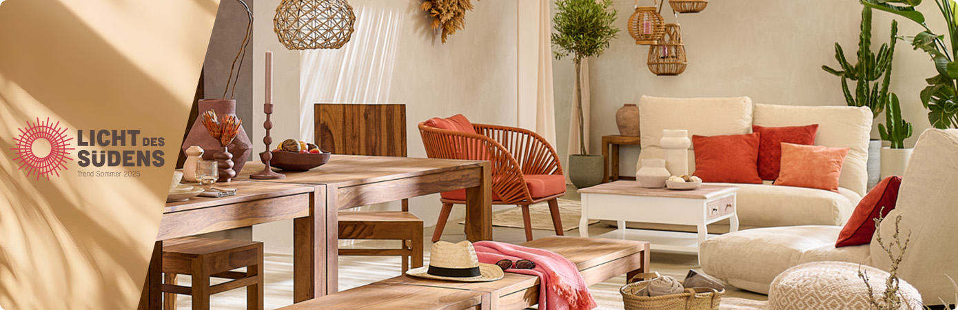 Licht des Südens, Trend Sommer 2025. Wohn/-Esszimmer mit zwei beigen Relaxliegen, terrakotta-farbene Kissen, Bodenkissen in Creme, weißer Couchtisch mit holzfarbener Tischplatte, Tischgruppe mit Esszimmertisch, Bank und zwei Stühlen in dunklem Holz. Glas- und Keramikaccessoires stehen auf den Tischen. 
